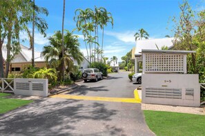 Una calle residencial con casas, palmeras y una entrada portonada.