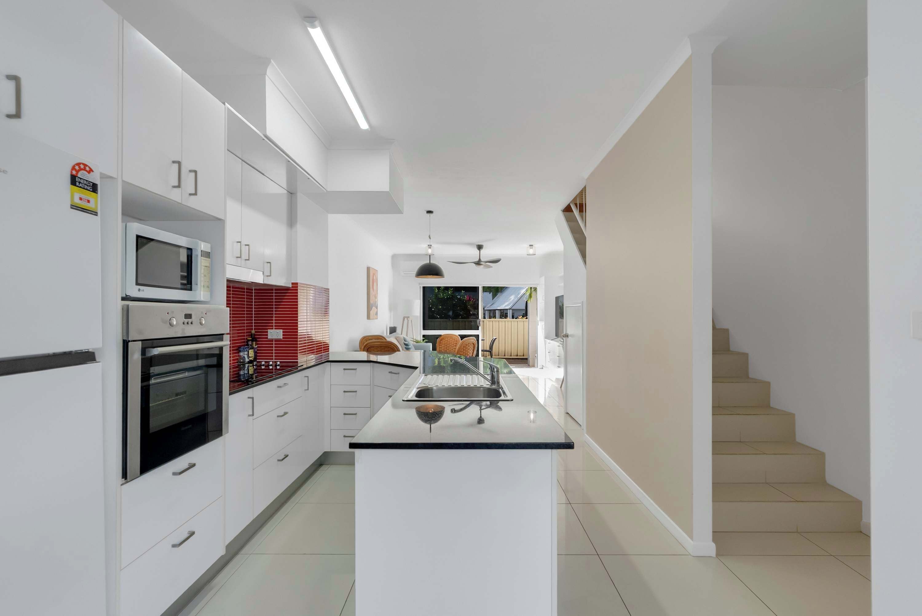A modern kitchen with white cabinetry, a central island, and a staircase leading to another level.