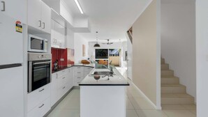 Une cuisine moderne avec des meubles blancs, un îlot central et un escalier menant à un autre niveau.