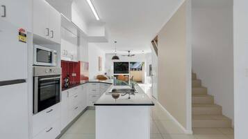 A modern kitchen with white cabinetry, a central island, and a staircase leading to another level.