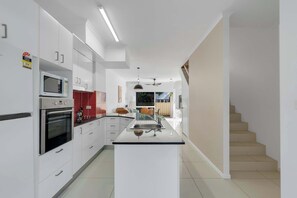 Una cocina moderna con armarios blancos, una isla central y una escalera que sube a otro nivel.