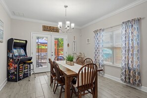 A dining area with a wooden table, chairs, a chandelier, a game console, and a window with patterned curtains. - Hot Tub/Fire Pit/Star Wars Room/Military Friendly (Navarre)