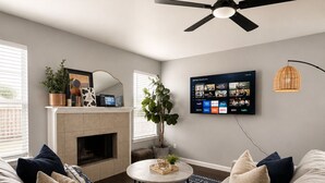 Ein modernes Wohnzimmer mit einer Eckcouch, einem Kamin, einem Deckenventilator und einem Wandfernseher, der verschiedene Kanäle zeigt.