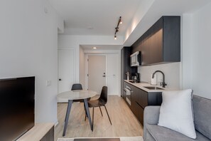 A modern kitchen with dark cabinetry, a built-in microwave, and a sink. There's a dining area with a round table and two chairs. - Stylish Sunlit Condo in Downtown Toronto (Toronto)