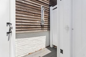 Eine weiße Tür mit einem Metallgriff, eine Wand aus Holzlatten und ein weißer Sockel aus Ziegelsteinen.
