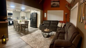 Una sala de estar con un sofá, una mesa de comedor con sillas, una zona de cocina con electrodomésticos y una chimenea.