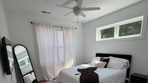 Une chambre à coucher avec un lit, un ventilateur de plafond, une fenêtre, un miroir et un tapis.