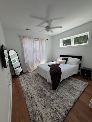 Ein Schlafzimmer mit Bett, Deckenventilator, Fenster, Spiegel und Teppich.