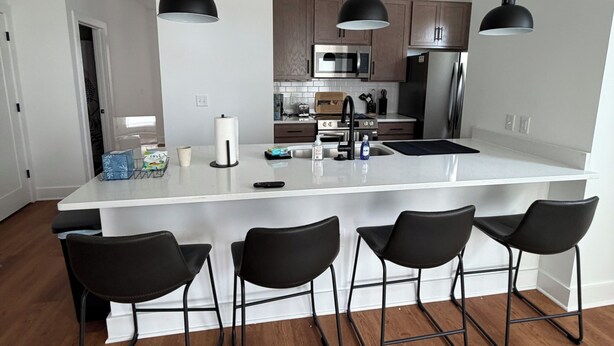 Une cuisine moderne dotée d’un îlot central, de tabourets de bar, de luminaires suspendus et d’appareils électroménagers en acier inoxydable.