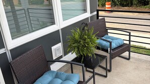 Un balcon avec deux fauteuils en osier, chacun agrémenté d’un coussin bleu, et une plante en pot.