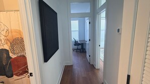Un couloir doté d’un plancher en bois, de murs blancs et d’une porte donnant sur une salle de bain avec des toilettes et un rideau de douche.