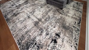 Un salon moderne avec un canapé d’angle, un coin repas doté de tabourets de bar et deux fenêtres donnant sur un paysage verdoyant.