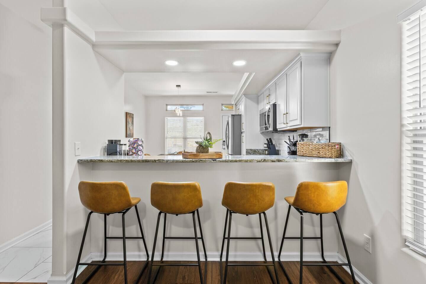 A kitchen with white cabinets, a granite countertop, and four yellow bar stools.