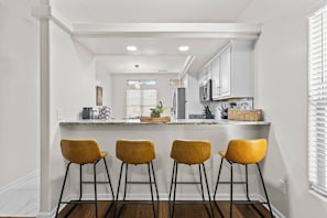 A kitchen with white cabinets, a granite countertop, and four yellow bar stools.