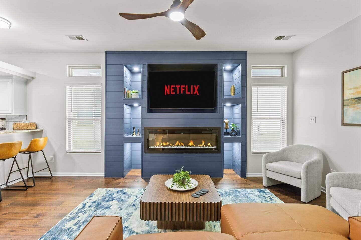 A living room with a fireplace, a TV mounted above it, and a ceiling fan.