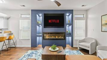 A living room with a fireplace, a TV mounted above it, and a ceiling fan.