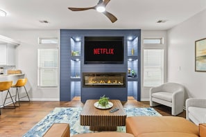 A living room with a fireplace, a TV mounted above it, and a ceiling fan.