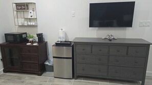 Una kitchenette equipada con microondas, cafetera, refrigerador y un televisor de pantalla plana montado en la pared.