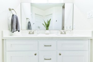 A bathroom with a white vanity, two sinks, a large mirror, and a potted plant.