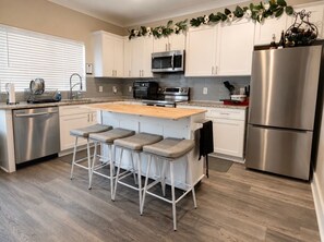 A modern kitchen with stainless steel appliances, a wooden island with bar stools, and a decorative plant overhead. - Westside Luxury Townhome - Close to Everything (Atlanta)