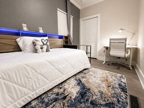 A bedroom with a bed, a desk, a chair, a lamp, and a window with curtains. - Westside Luxury Townhome - Close to Everything (Atlanta)