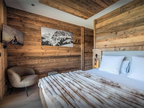 Una habitación con paneles de madera, una cama, una silla y un cuadro en la pared.