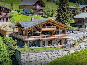 Un chalé grande de madera con balcón, base de piedra y vistas de casas circundantes.