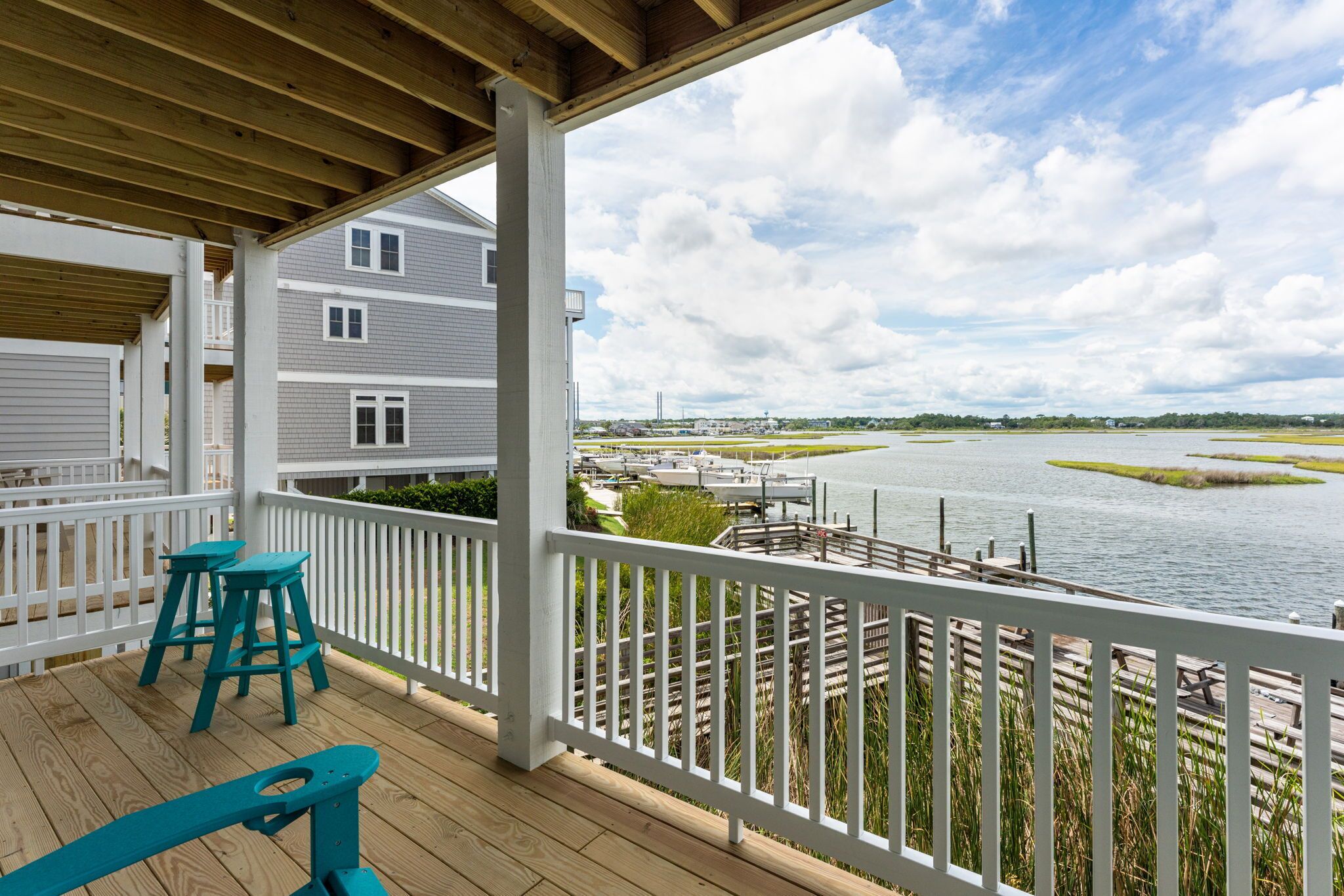 A covered deck with two stools, overlooking a body of water with docks and buildings in the background.