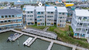 A waterfront property with multiple-story buildings, docked boats, and a pier. - Waterfront Paradise, 5BR, Elevator, Expansive Decks & Views (Surf City)
