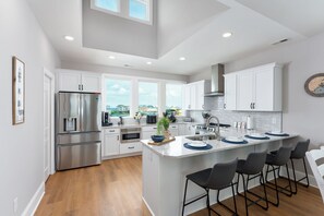 Una cocina moderna con armarios blancos, electrodomésticos de acero inoxidable, una isla grande con taburetes de bar y vistas al exterior.