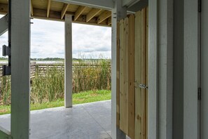 Un espacio al aire libre techado con piso de concreto, puerta de madera y vista a un campo cubierto de césped.