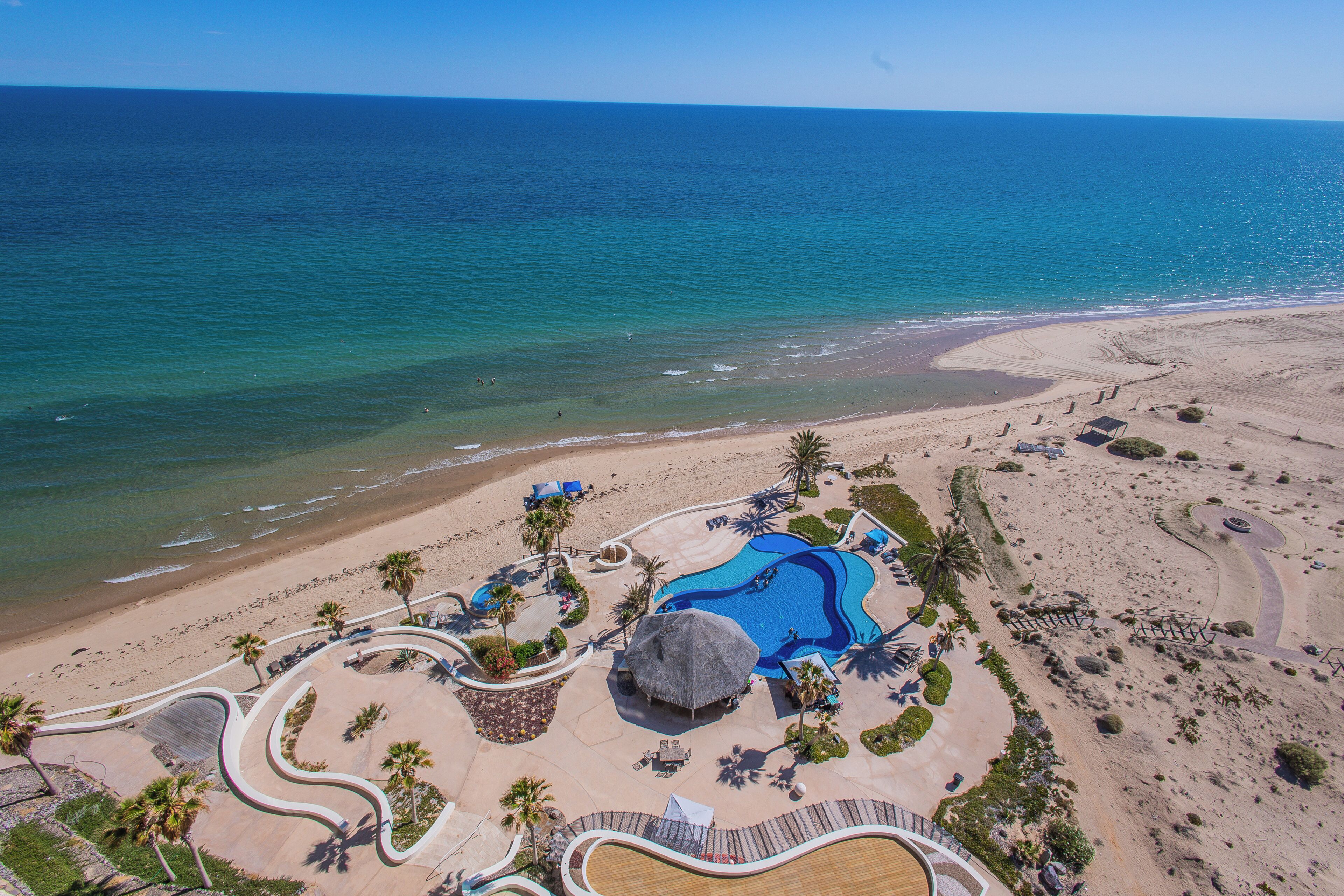 A resort with a large swimming pool, palm trees, and a beach.
