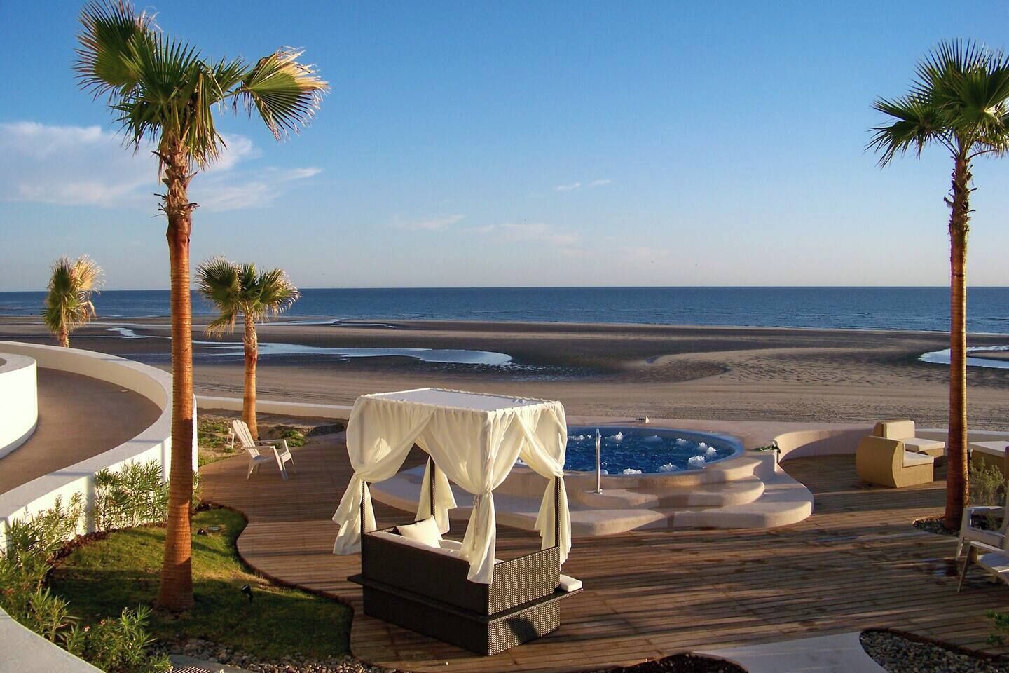 A poolside area with a hot tub, lounge chairs, and a view of the beach.