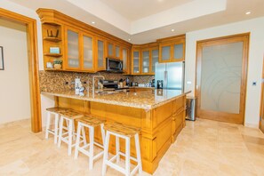 A kitchen with wooden cabinets, a stainless steel refrigerator, a microwave, and a granite countertop. - Amazing Beachfront Condo, Tessoro at Las Conchas, Puerto Penasco (Las Conchas)