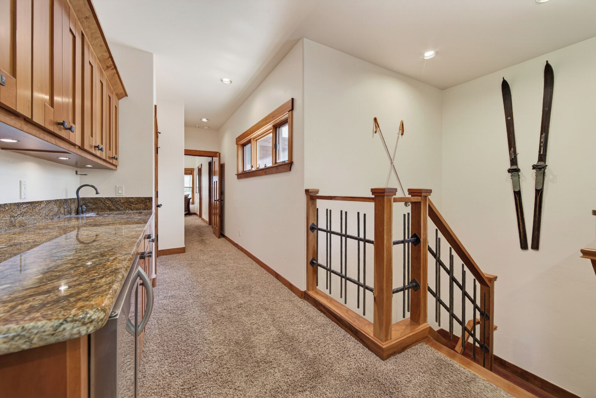 A kitchen with granite countertops, wooden cabinets, and a hallway leading to a staircase.