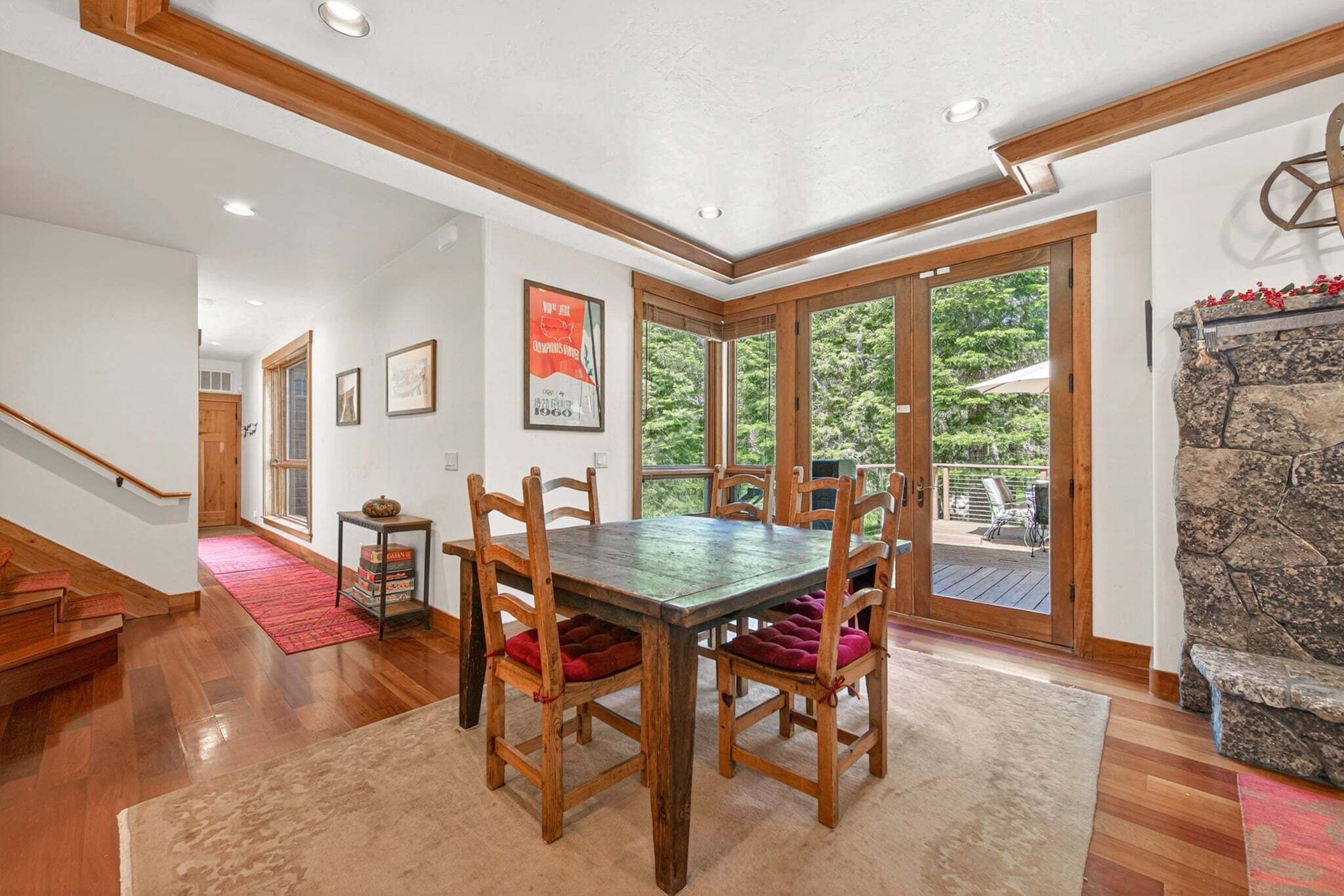 A dining area with a wooden table and chairs, a stone fireplace, and a view of the outdoors.