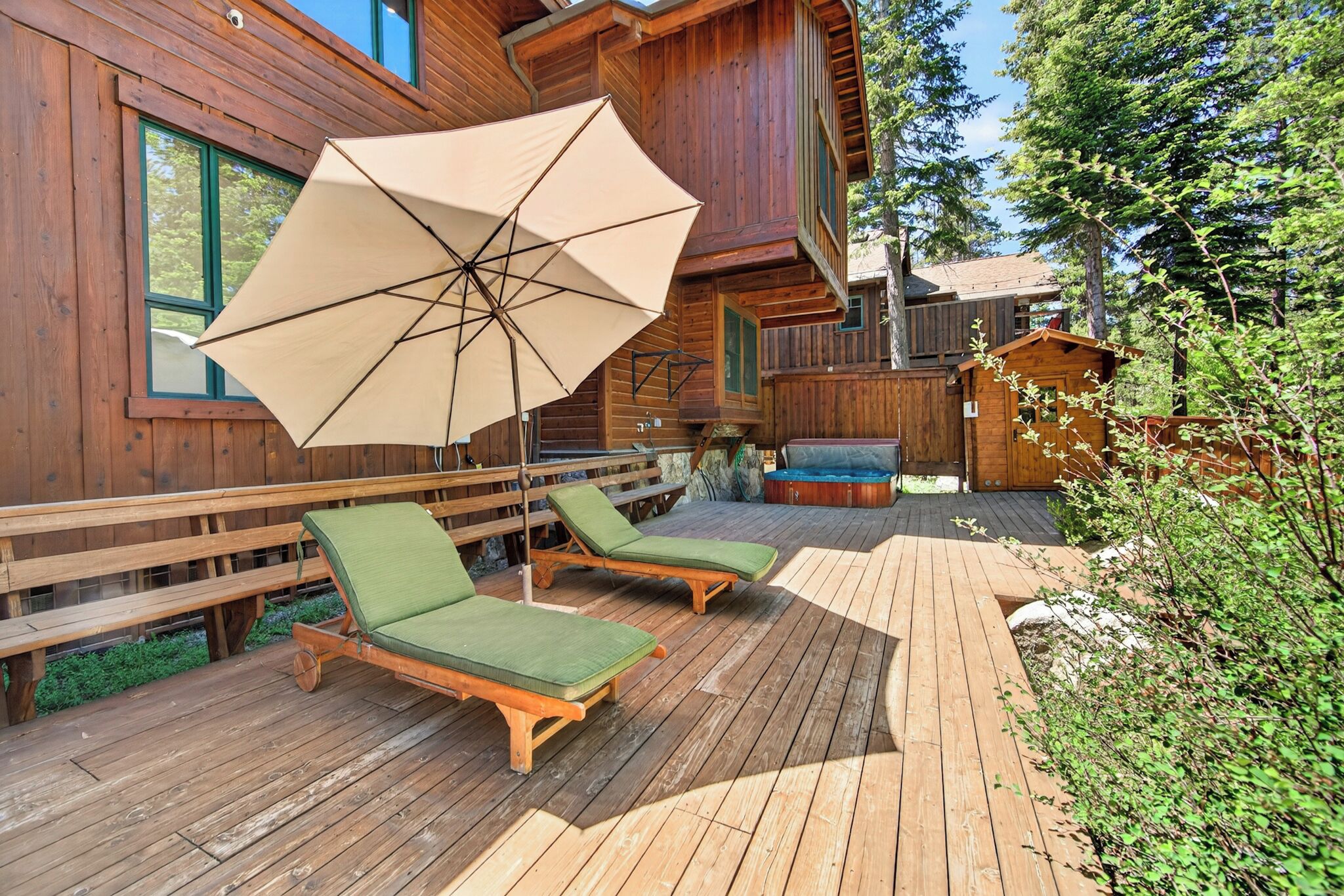Una terraza de madera con sillones de descanso y una sombrilla, rodeada por una valla de madera y árboles.