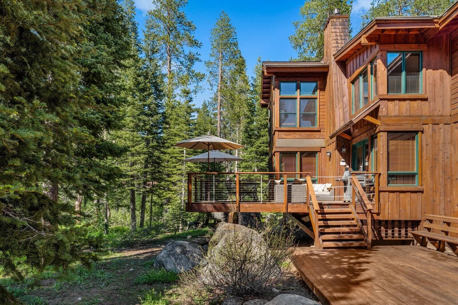 A wooden cabin with a deck, surrounded by trees.