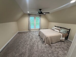 A bedroom with a bed, a ceiling fan, a window with curtains, and a carpeted floor.