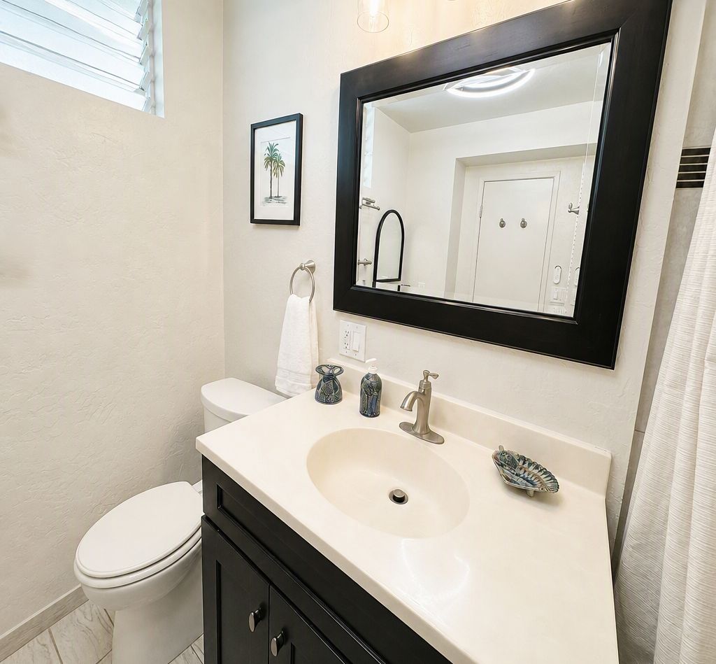 A bathroom with a white toilet, a sink with a mirror above it, and a framed picture on the wall.