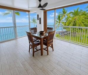 A balcony with a dining table and chairs, overlooking a tropical beach and ocean.