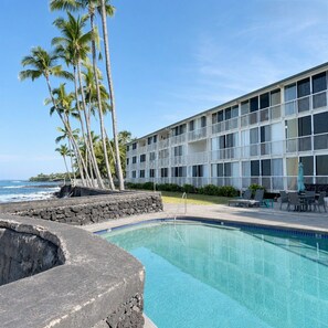 A hotel with a pool, palm trees, and ocean views. - KONA MAGIC SANDS 314 - Top Floor Oceanfront Corner Penthouse - Magic Sands Beach (Kailua-Kona)