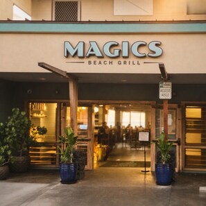 The exterior of a beach grill named 'MAGICS' with a 'NO PARKING ACCESS AISLE' sign. - KONA MAGIC SANDS 314 - Top Floor Oceanfront Corner Penthouse - Magic Sands Beach (Kailua-Kona)