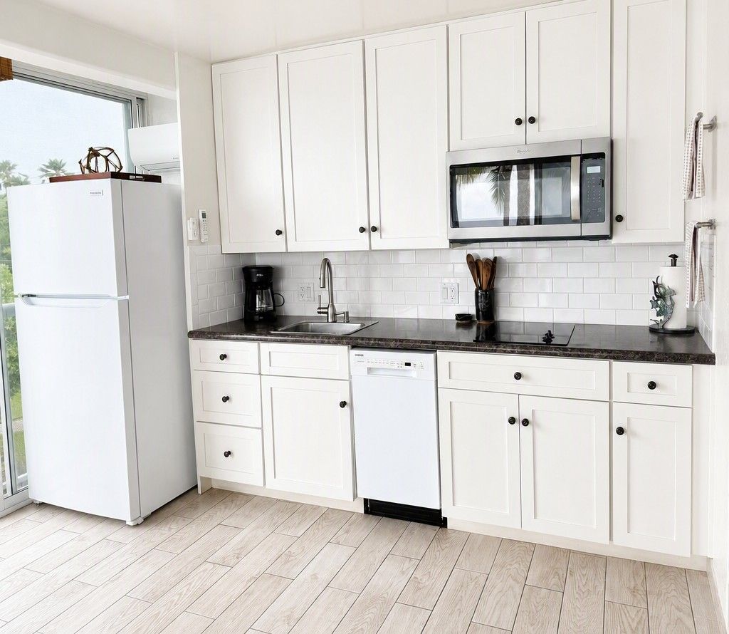 A modern kitchen with white cabinets, a built-in microwave, a dishwasher, and a window providing a view of the outdoors.