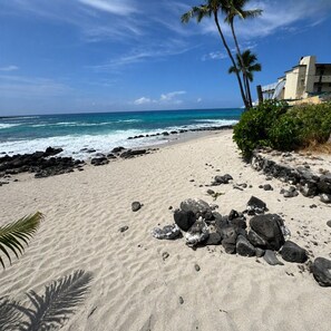 A beach with a rocky shoreline, palm trees, and a building with a balcony.