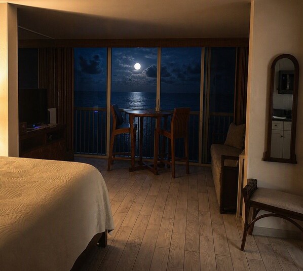 A hotel room with a balcony, a bed, a table, and chairs. - KONA MAGIC SANDS 314 - Top Floor Oceanfront Corner Penthouse - Magic Sands Beach (Kailua-Kona)
