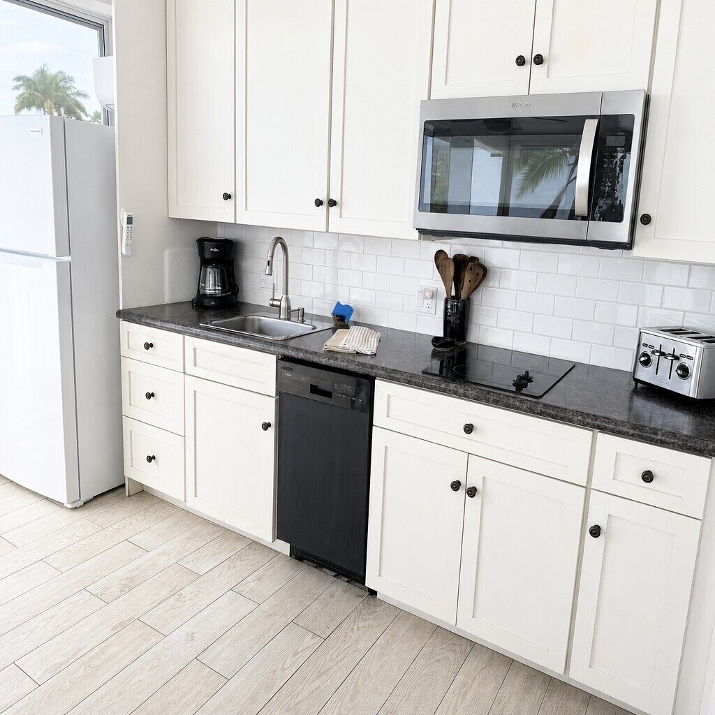 A kitchen with white cabinets, a stainless steel microwave, a dishwasher, a coffee maker, and a toaster.