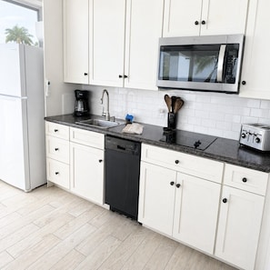 A kitchen with white cabinets, a stainless steel microwave, a dishwasher, a coffee maker, and a toaster.