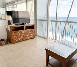 A balcony with a view of the sea, a wooden entertainment unit with a TV, and a glass table.