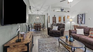Ein geräumiges Wohnzimmer mit Flachbildfernseher, Deckenventilator, Essbereich mit Tisch und Stühlen sowie eine gemütliche Sitzecke mit Sofa und Sesseln.